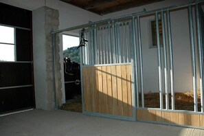 A stable with a wooden gate and metal bars, hay on the ground, and a mountain in the background. - Holiday apartment with 1 bedroom (Gohrisch OT Papstdorf)