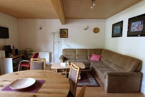 A living room with a wooden table, a sofa, a chair, and a television.