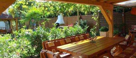 An outdoor wooden deck with a dining table and chairs, surrounded by lush greenery and a wooden fence.