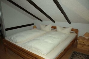 A twin bed with a wooden frame and white bedding in a room with sloped ceilings and exposed beams. - Mengelberg in the Leipzig New Lake District (Markkleeberg)