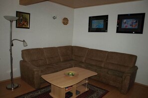 Une pièce d’angle avec un canapé marron, une petite table en bois, un lampadaire et des tableaux encadrés accrochés au mur.