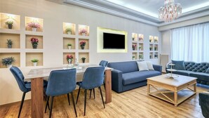 Uma sala de estar moderna com área de jantar, um sofá cinza, mesa de centro e TV na parede.