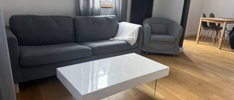 Una sala moderna con un sofá gris, una mesa de centro blanca y un sillón gris.