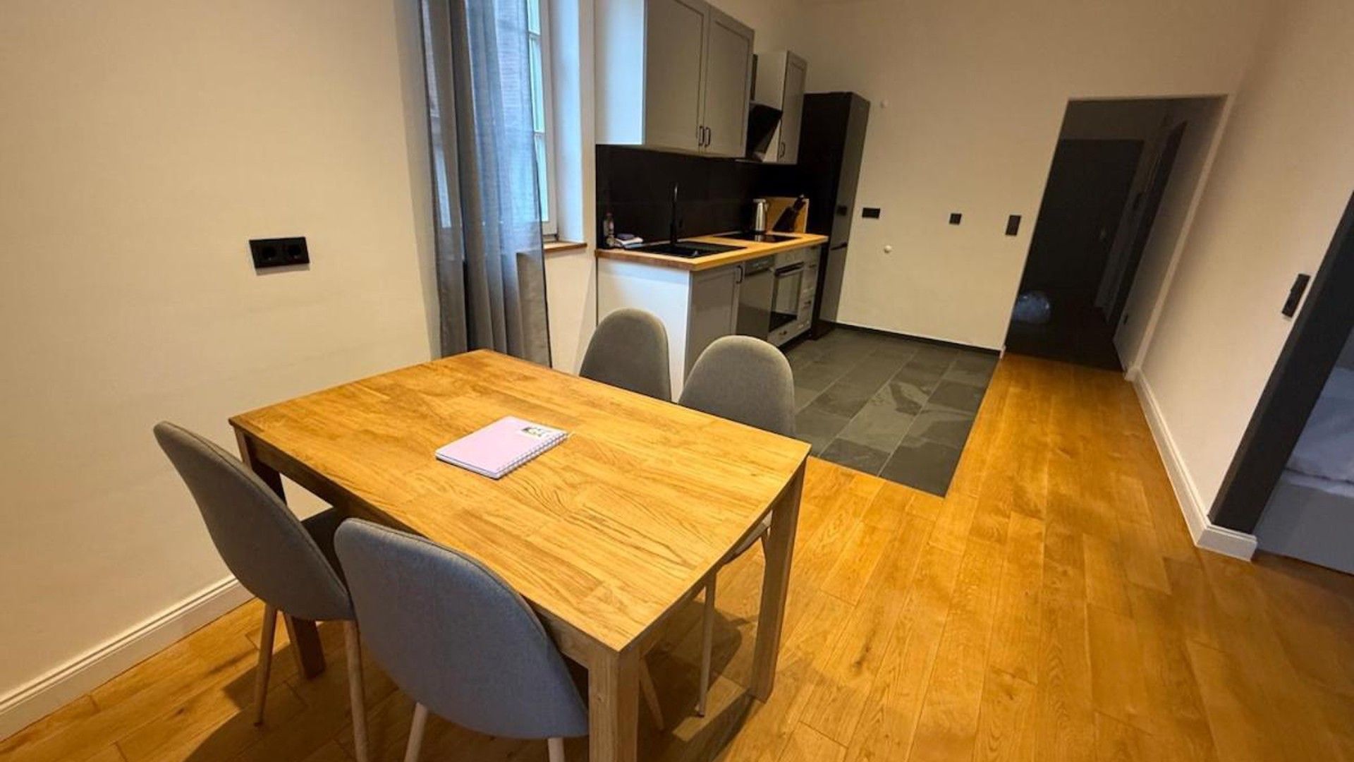 Eine kleine Küche mit modernen Geräten, ein Essbereich mit Holztisch und Stühlen sowie ein Flur, der in einen weiteren Raum führt.
