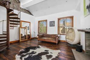 Ein geräumiges Zimmer mit einer Holztreppe, einem Ledersofa, einem Kuhfellteppich und einem einzigartigen, ei-förmigen Sessel.