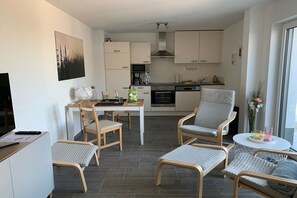 Ein modernes Wohnzimmer mit Essbereich, Küche und einem großen Fenster, das für natürliches Licht sorgt.
