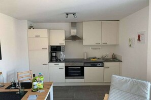 Eine kleine Küche mit weißen Schränken, einer Mikrowelle, einem Backofen und einem Spülbecken.