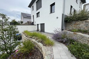 A modern two-story house with a stone retaining wall and a paved pathway. - Holiday apartment in Bad Bellingen with Wi-Fi (Bad Bellingen)