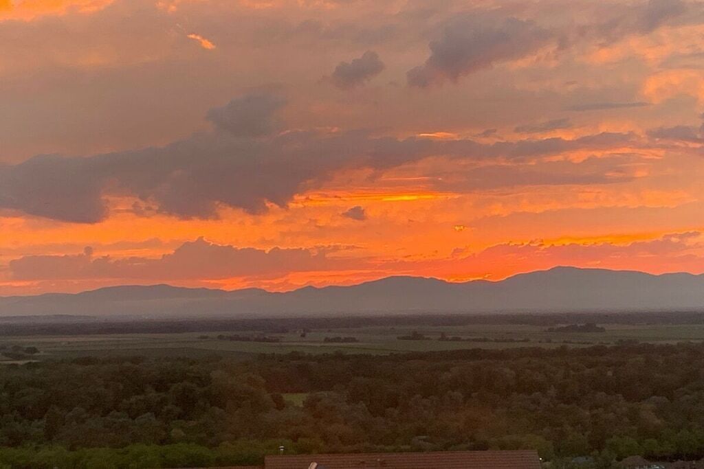A sunset over a mountainous landscape with a house in the foreground.