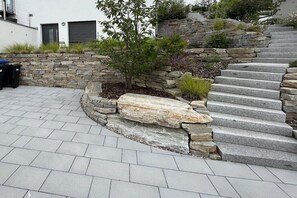 Eine Steintreppe führt zu einem Gebäude mit modernem Design, umgeben von einem angelegten Garten mit verschiedenen Pflanzen.