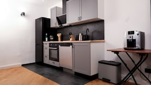 Una cocina moderna con armarios grises, horno empotrado, cafetera y cubo de basura.