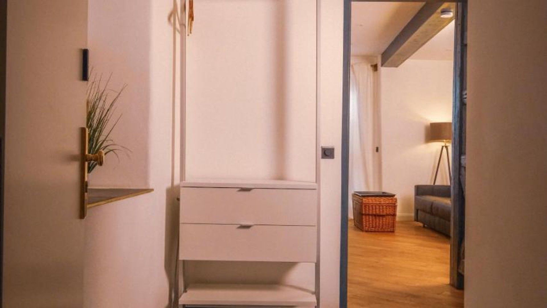 Ein Flur mit einem weißen Schrank, einer Pflanze und einem Korbwäschesammler.