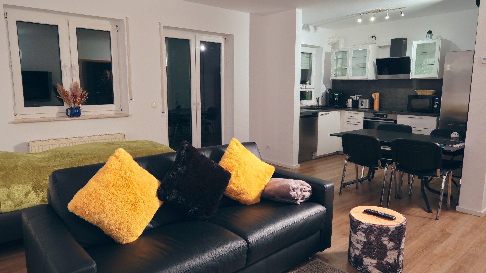 A modern living room with a black leather sofa and a dining area with a black table and chairs.