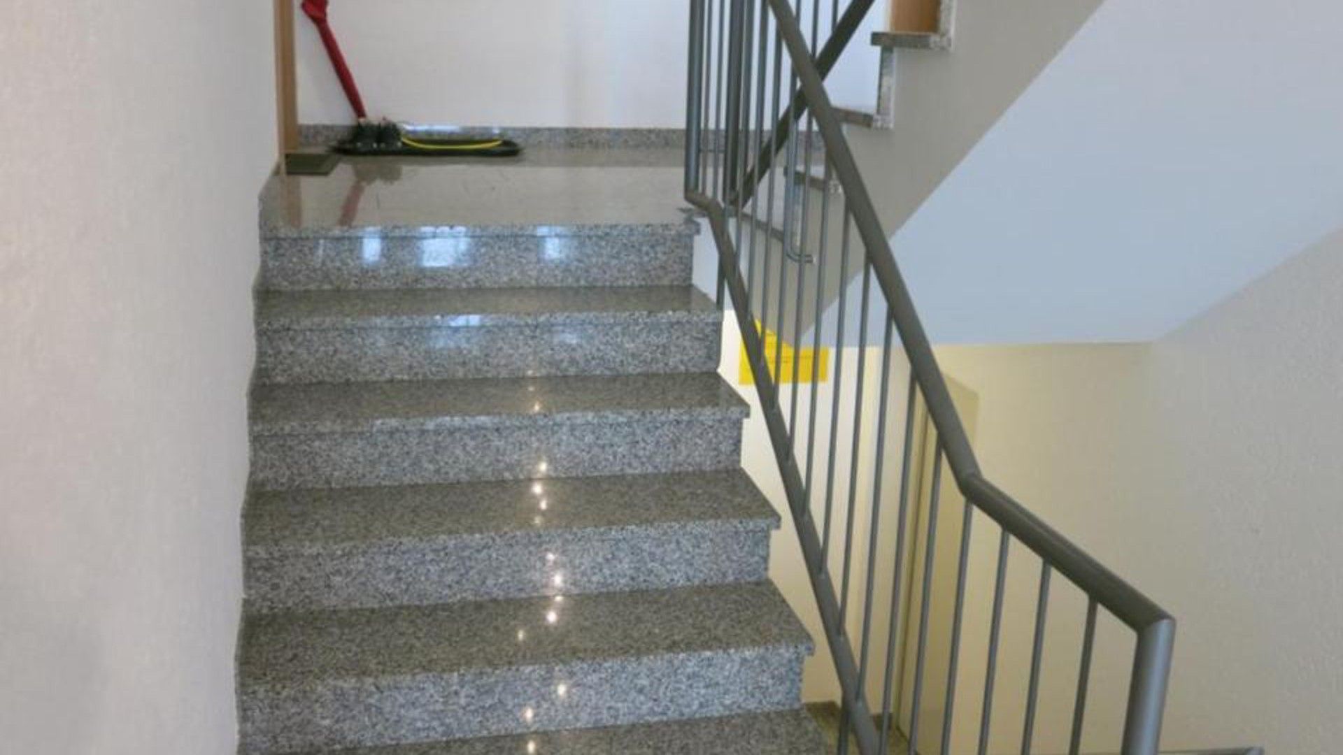 Un escalier avec une rampe en métal, menant à un palier.