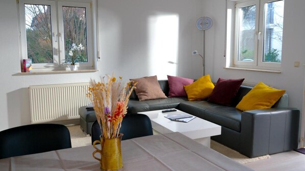 Ein modernes Wohnzimmer mit einem grauen Sofa, bunten Kissen, einem weißen Couchtisch und einer Vase mit Trockenblumen.