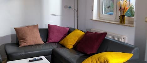Una sala de estar moderna con un sofá gris, una mesa de centro blanca y un ventanal con vistas a zonas verdes.