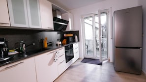 Eine moderne Küche mit weißen Schränken, einem Edelstahl-Kühlschrank und einer Glastür zum Balkon.