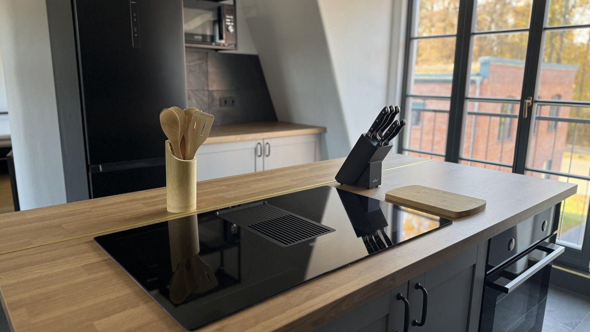 A modern kitchen with a built-in induction cooktop, a knife block, and a wooden cutting board on a sleek countertop.