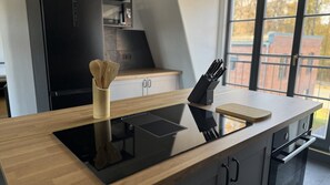 Una cocina moderna con placa de inducción integrada, un bloque de cuchillos y una tabla de cortar de madera sobre una encimera elegante.