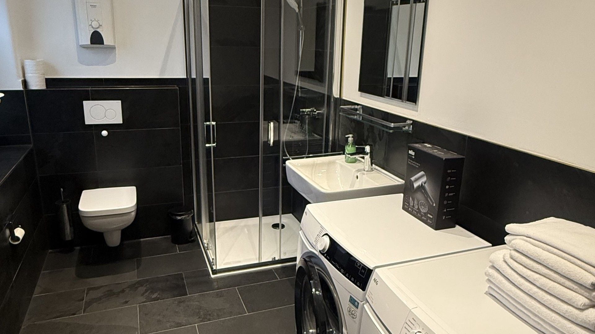 A modern bathroom with a glass shower enclosure, a white sink, and a washing machine.