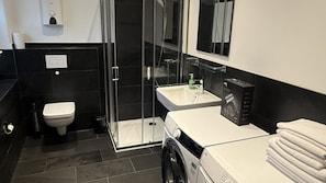 Un baño moderno con cabina de ducha de vidrio, un lavamanos blanco y una lavadora.