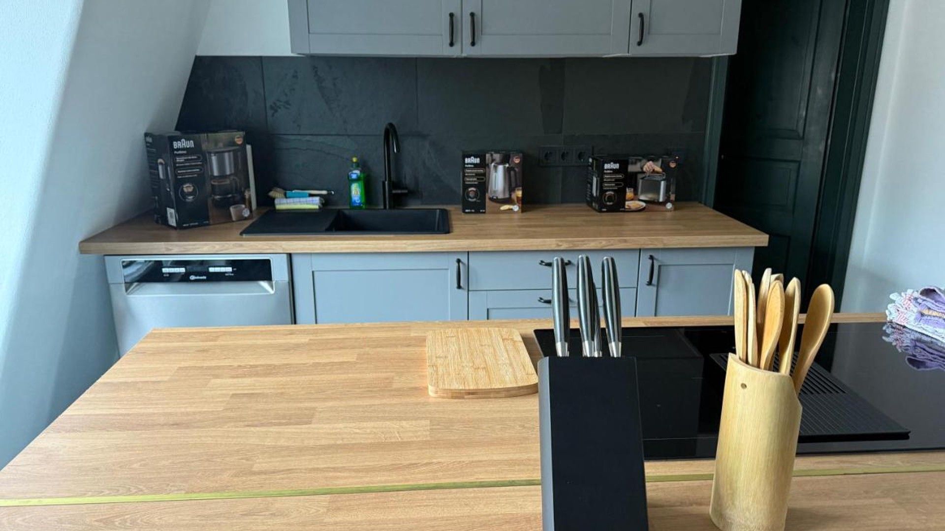 Eine moderne Küche mit grauen Schränken, einer Holzarbeitsplatte und verschiedenen Geräten, darunter eine Kaffeemaschine und ein Toaster.