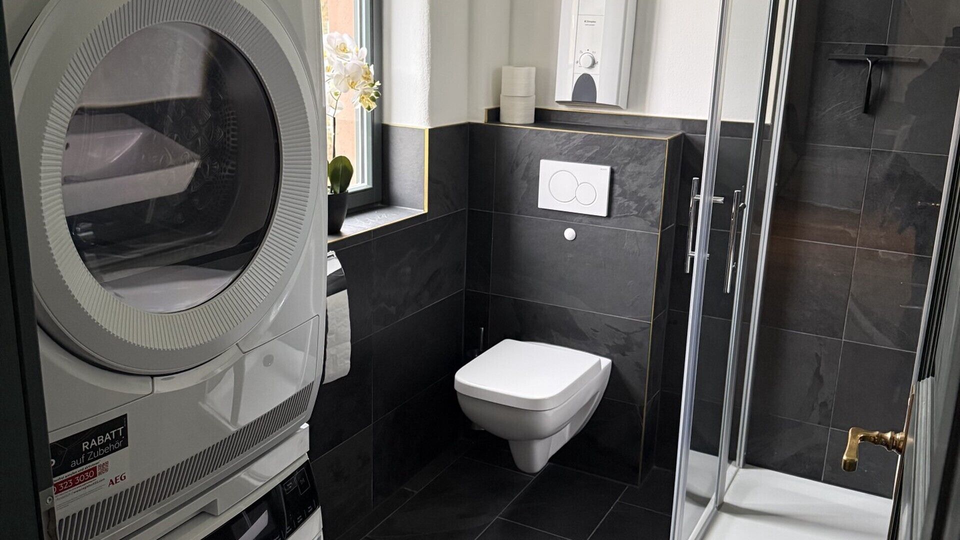 Et lille badeværelse med en indbygget vaskemaskine, toilet og bruseniche.