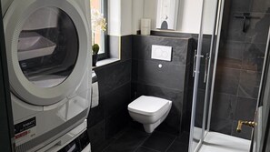Un baño pequeño con lavadora incorporada, inodoro y cabina de ducha.