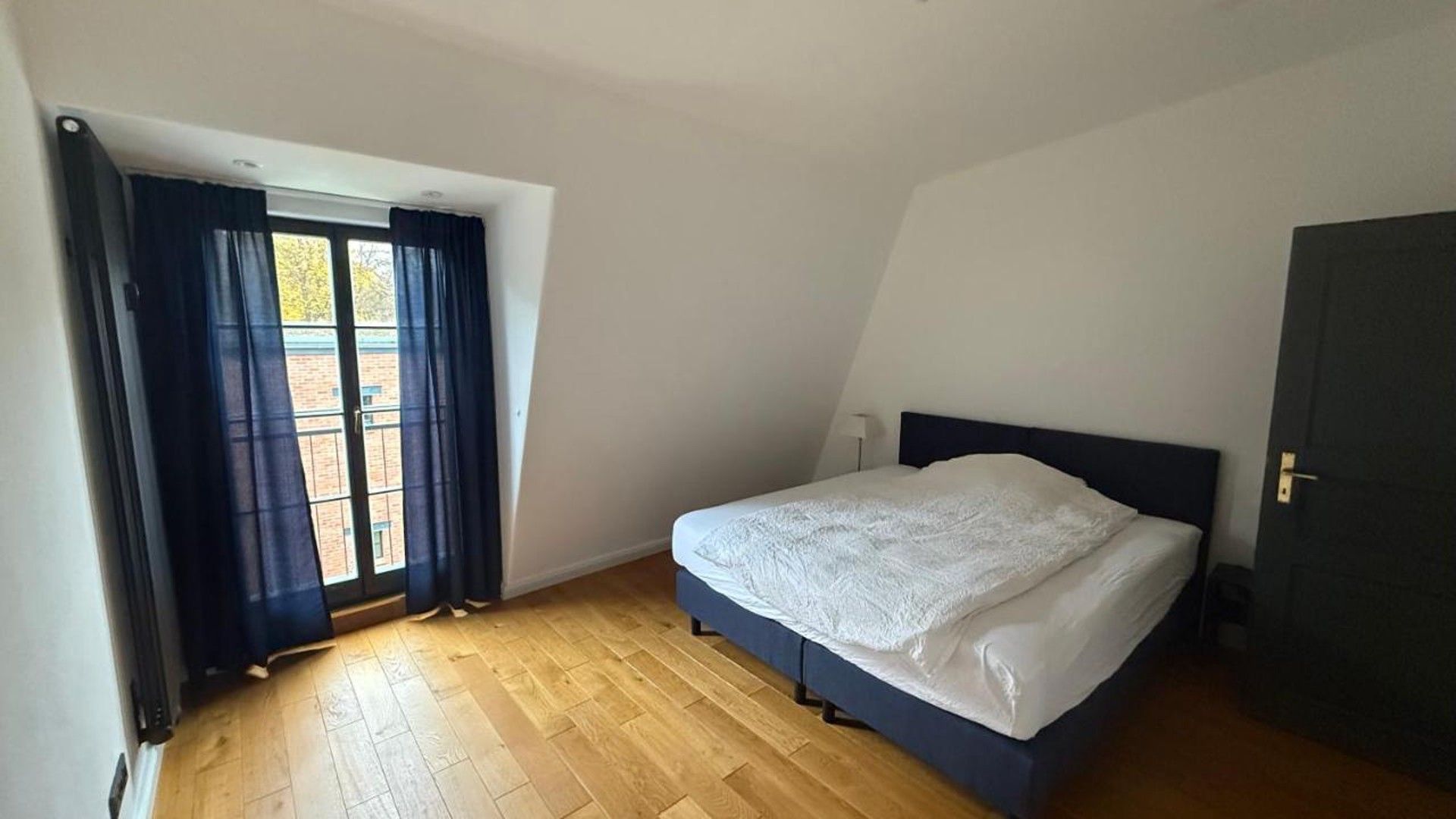 Un dormitorio con cama, ventana con cortinas y una puerta.