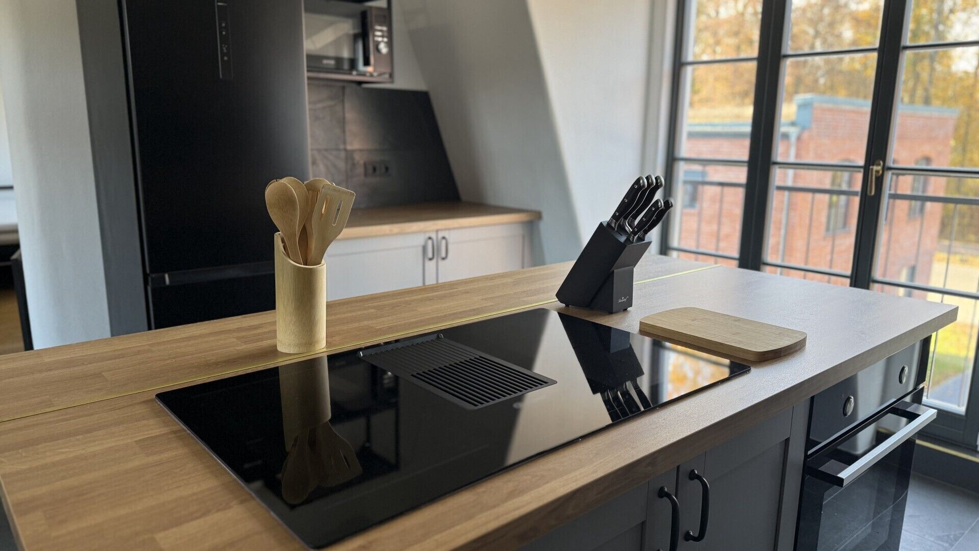 Une cuisine moderne dotée d’une plaque de cuisson à induction intégrée, d’un bloc à couteaux et d’une planche à découper en bois, le tout posé sur un plan de travail élégant.