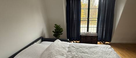 Un dormitorio con cama, ventana con cortinas y una planta.