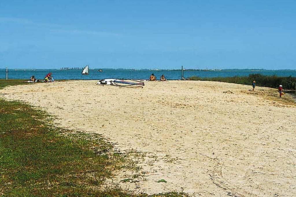 Ein sandiger Strand mit einem Segelboot, Menschen und einem entfernten Steg.
