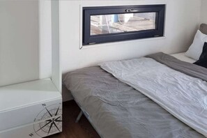 A single bed with a grey mattress and white bedding, a small window with a black frame, and a white bedside table with a compass design. - Houseboat in Anjum with swimming pool (Anjum)