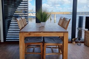 A wooden dining table with four chairs, a potted plant, and a view of a dock and water. - Houseboat in Anjum with swimming pool (Anjum)