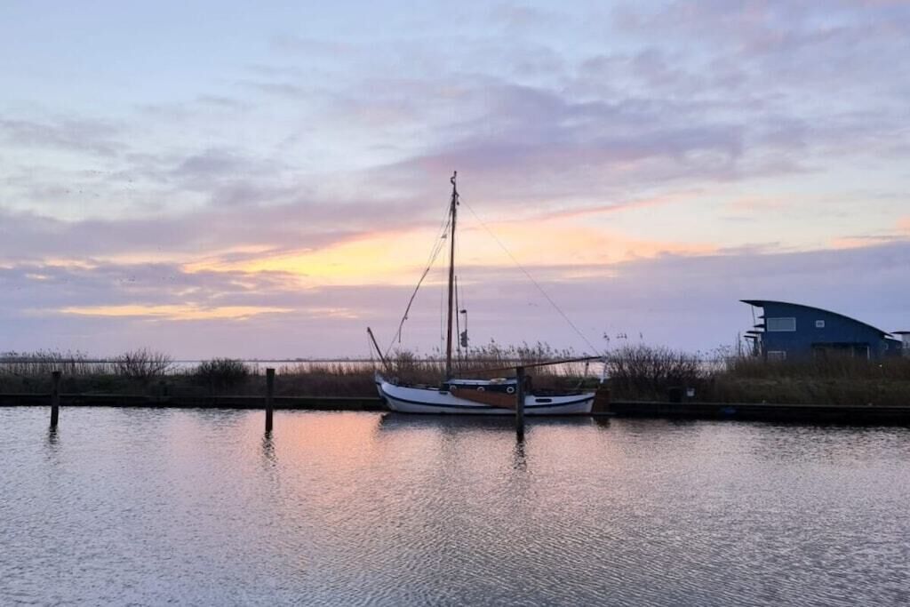 A calm body of water with a boat docked at a pier, a building with a curved roof in the background, and a sunset sky.