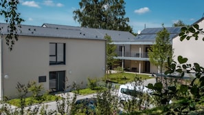 Ein modernes Gebäude mit flachem Dach, einem Balkon und einem kleinen Garten.