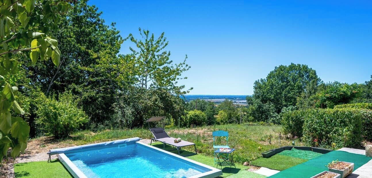 A swimming pool with a view of the sea, surrounded by greenery and a lawn.