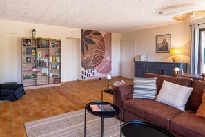 Una sala de estar con un sofá marrón, una mesa de centro, una estantería y una decoración abstracta de gran tamaño en la pared.
