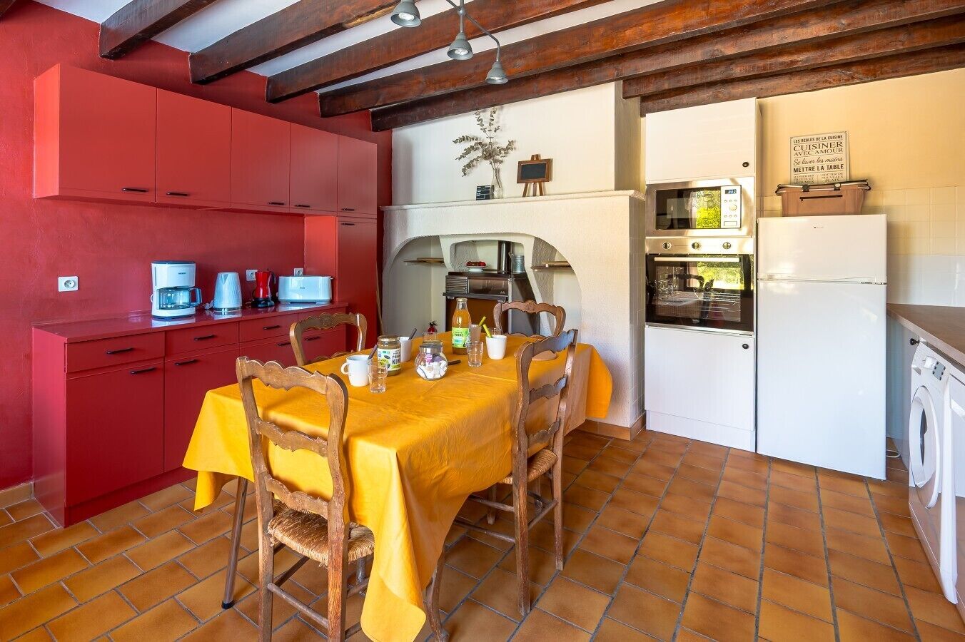 Una cocina compacta con armarios rojos, una mesa de comedor con mantel amarillo y una lavadora.
