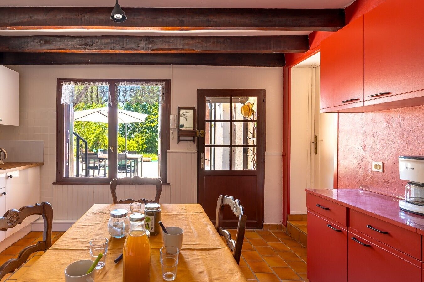 A dining area with a table set for two, a window with a view of the outdoors, and red cabinetry.