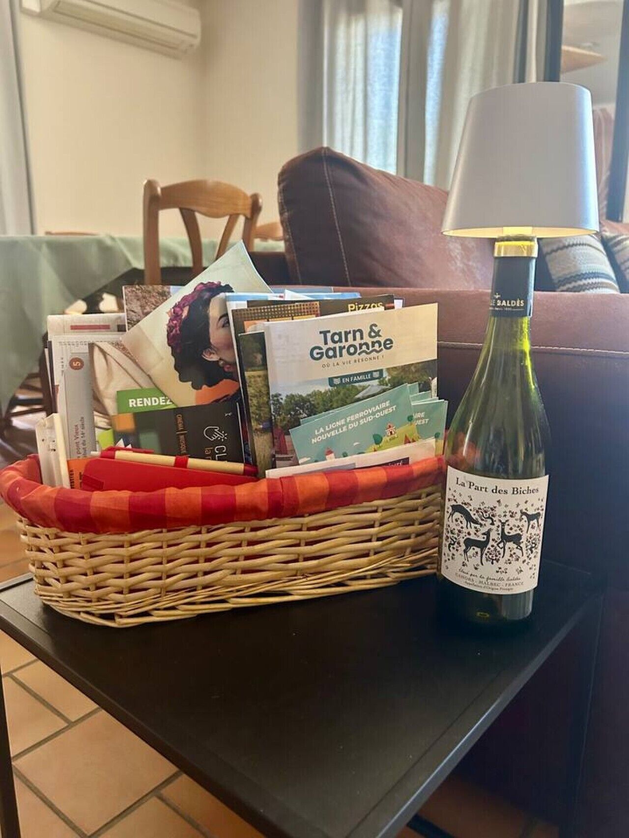 Un panier en osier rempli de magazines et une bouteille de vin, posés sur une table.