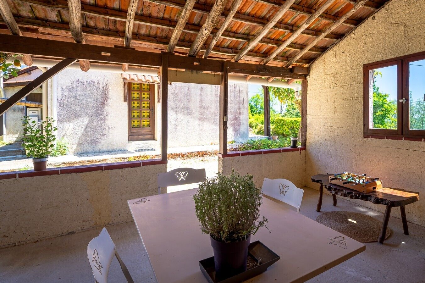 A covered outdoor seating area with a table, chairs, and a foosball table.