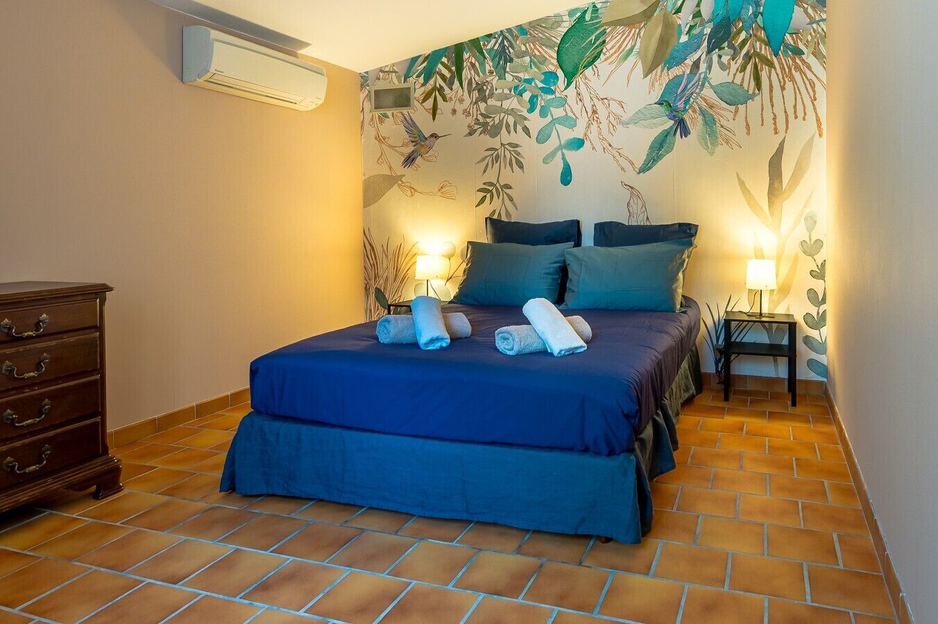 A bedroom with a bed, two bedside tables, a dresser, and a wall with a leaf pattern.