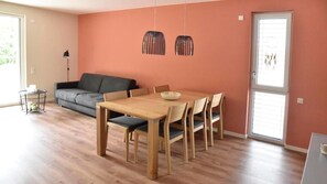 Ein Essbereich mit Holztisch und Stühlen, einem grauen Sofa und einer Stehlampe.