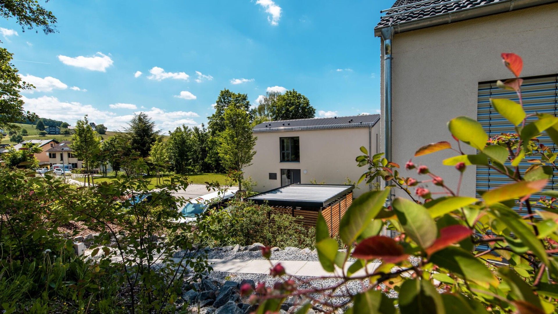 A residential building with a flat roof, a visible garage, and a garden area with trees and shrubs.