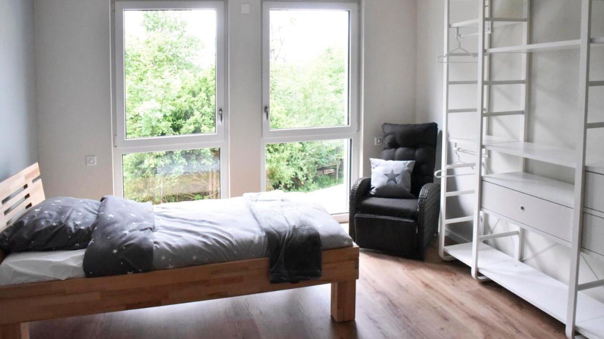 A bedroom with a bed, a chair, and a white wardrobe.
