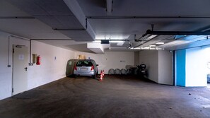 Eine Parkgarage mit einem Auto in der Mitte, Feuerlöschern und einer blauen Tür rechts.