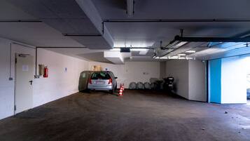 Eine Parkgarage mit einem Auto in der Mitte, Feuerlöschern und einer blauen Tür rechts.