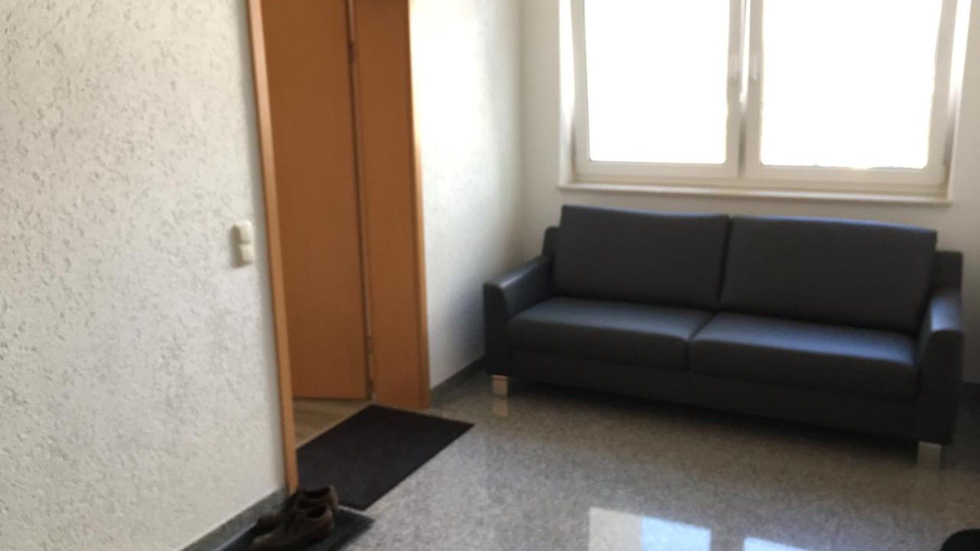 A room with a grey sofa, a door, and a window.