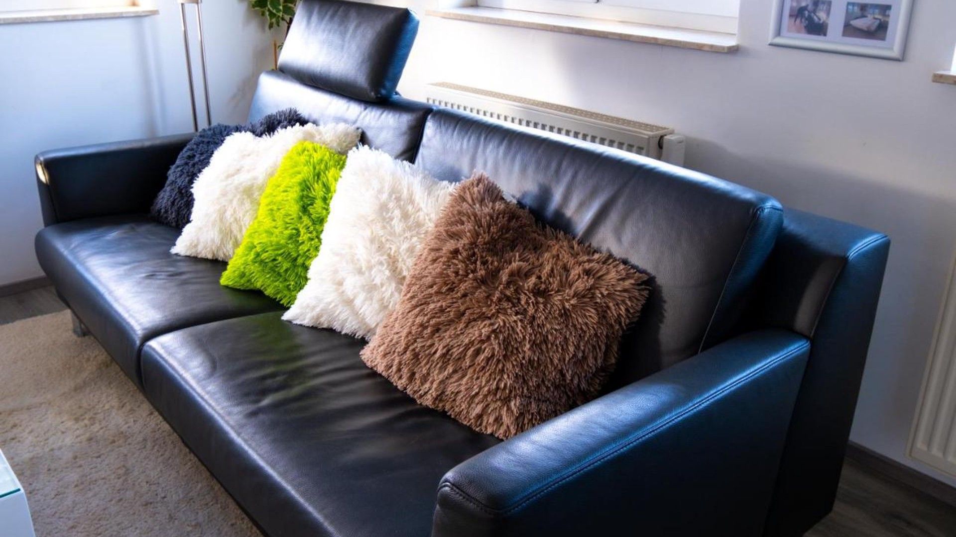 Ein schwarzes Ledersofa mit drei flauschigen Kissen in verschiedenen Farben.